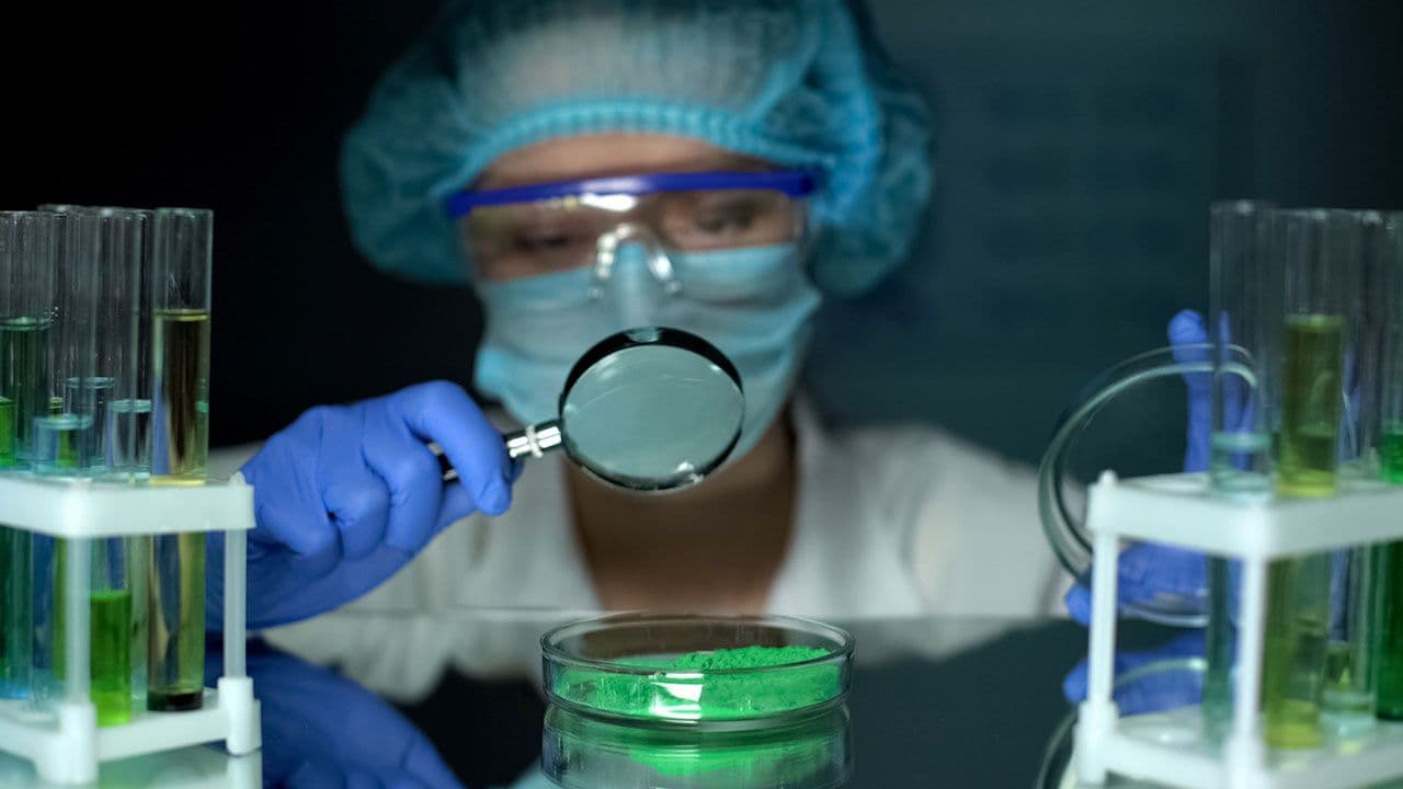 Researcher analyzing green powder pigment in petri dish with magnifying glass | Image Credit: ©motortion – stock.adobe.com