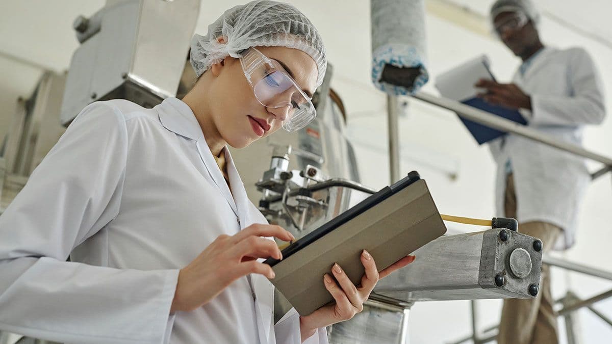 Side view portrait of pretty young woman wearing lab coat and using digital tablet in modern factory workshop, copy space |©Seventyfour - stock.adobe.com