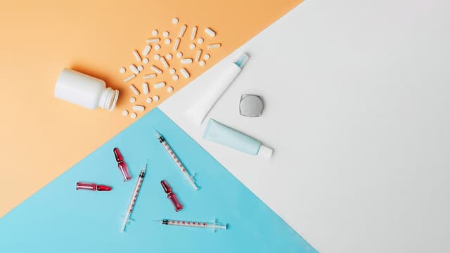 Mock-up cosmetic tubes, bottle with spilled tablets and syringes with ampules on white, orange and blue background. Cosmetology vs medicine concept. Flat lay.|Image Credit: © LanaUst - © LanaUst - stock.adobe.com