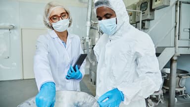 Medium shot of female process supervisor in lab coat pointing at equipment controlling production quality with African American male manufacturing technician, working in protective suit at factory | Image Credit: © Seventyfour - © Seventyfour - stock.adobe.com