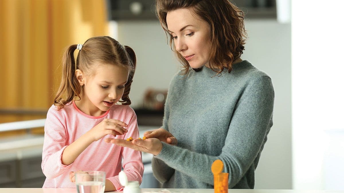 Young woman giving pill to her daughter at table | Image Credit: ©Pixel-Shot - stock.adobe.com